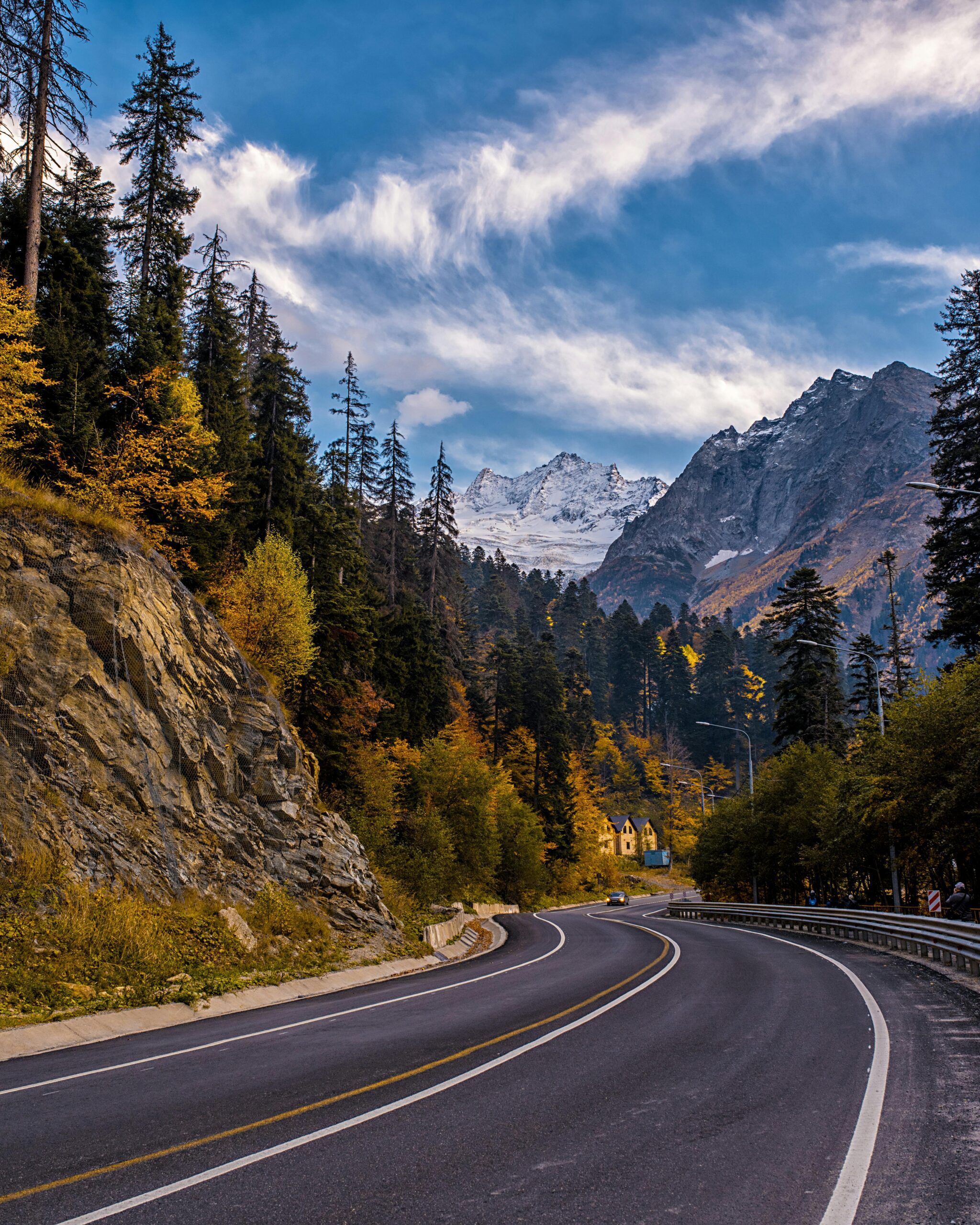 A picturesque mountain road with vibrant autumn colors and majestic snow-capped peaks.