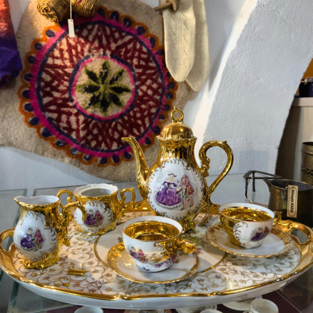 An elegant Turkish tea set with gold accents on a decorative tray, accented by a vibrant wall tapestry.