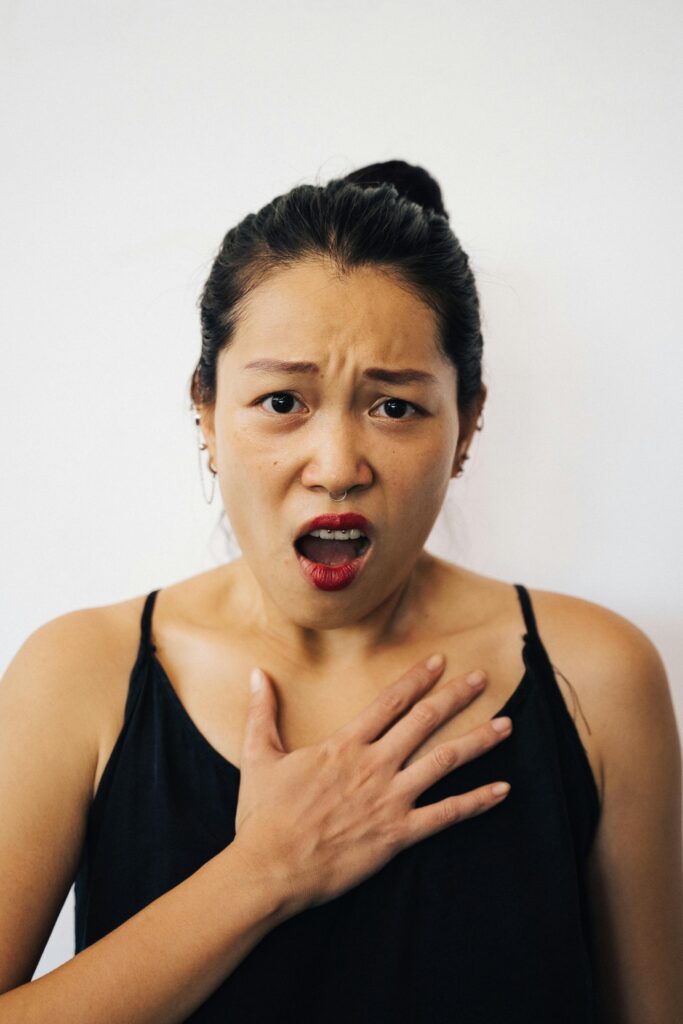 A woman in a black top looks surprised, showcasing a shocked expression with her hand on her chest.